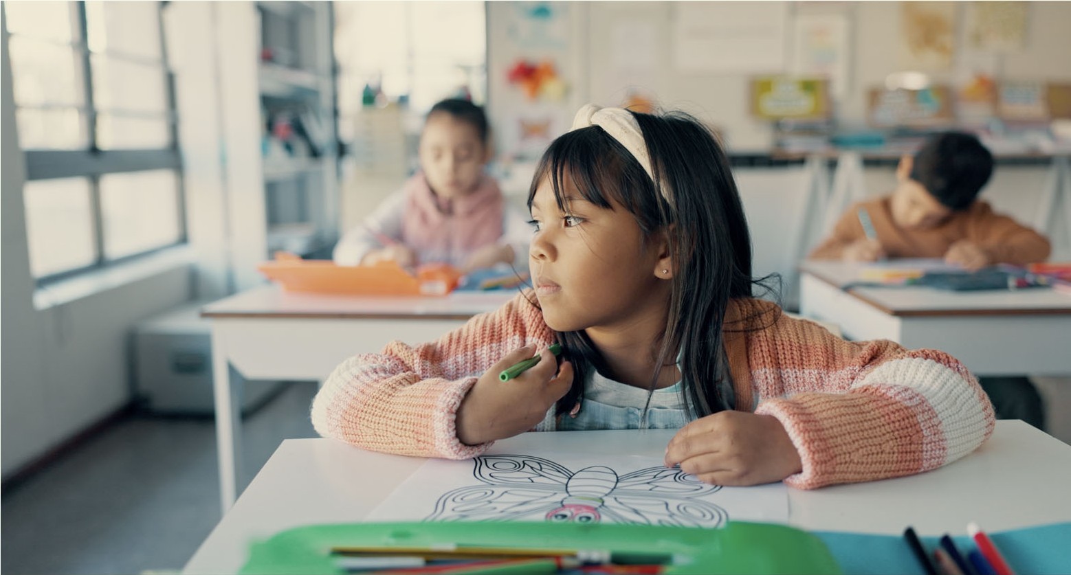 Child looking away while seated at a classroom desk